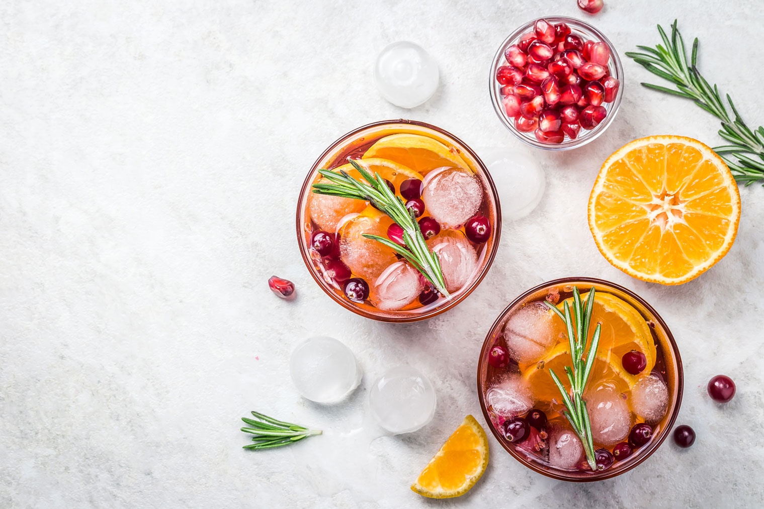 Two holiday-inspired cocktails with pomegranate arils and a sliced orange.
