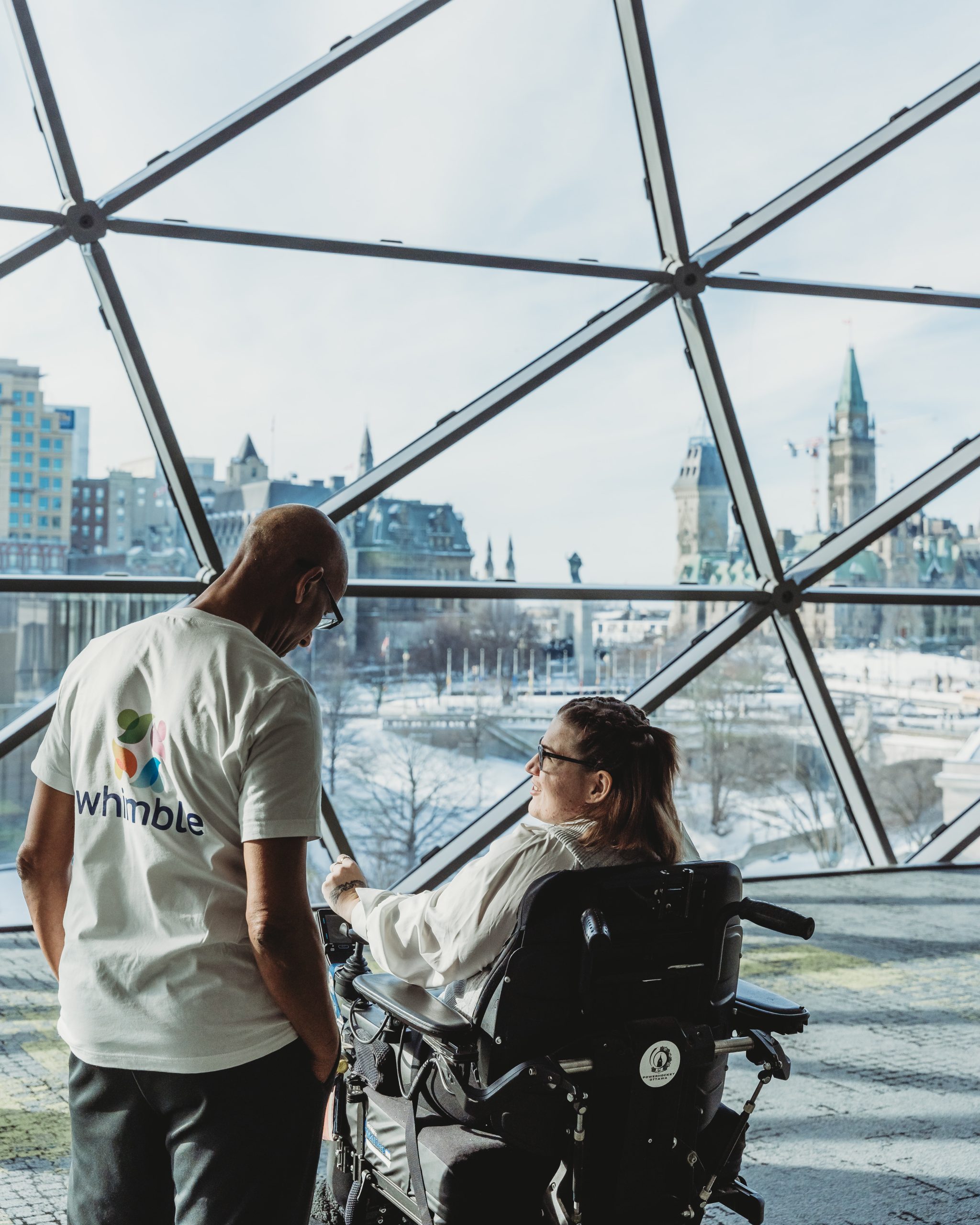 man and women in wheelchair looking at view of parliament from parliament foyer at the Shaw Centre